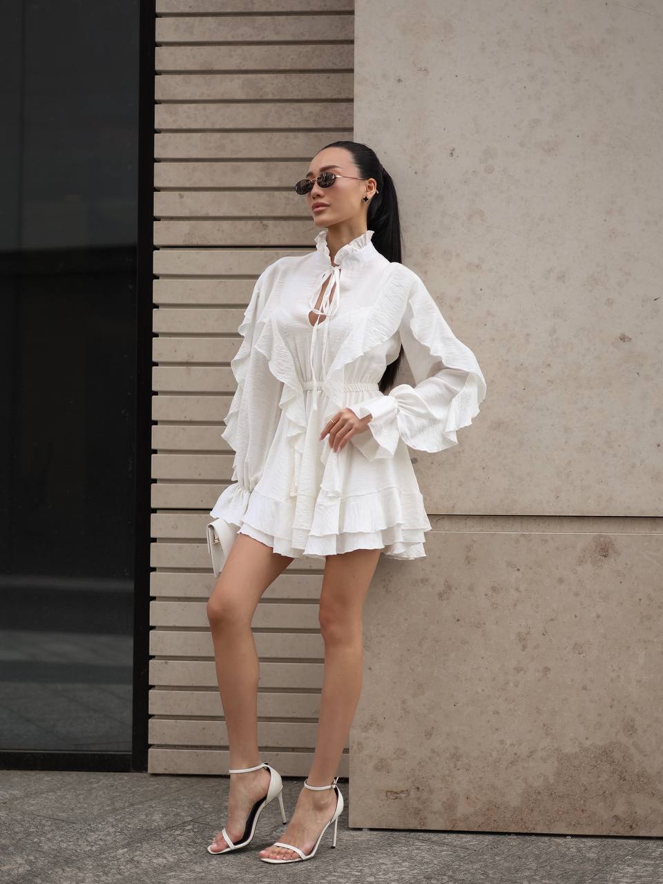 Woman wearing a white dress standing against a neutral wall.