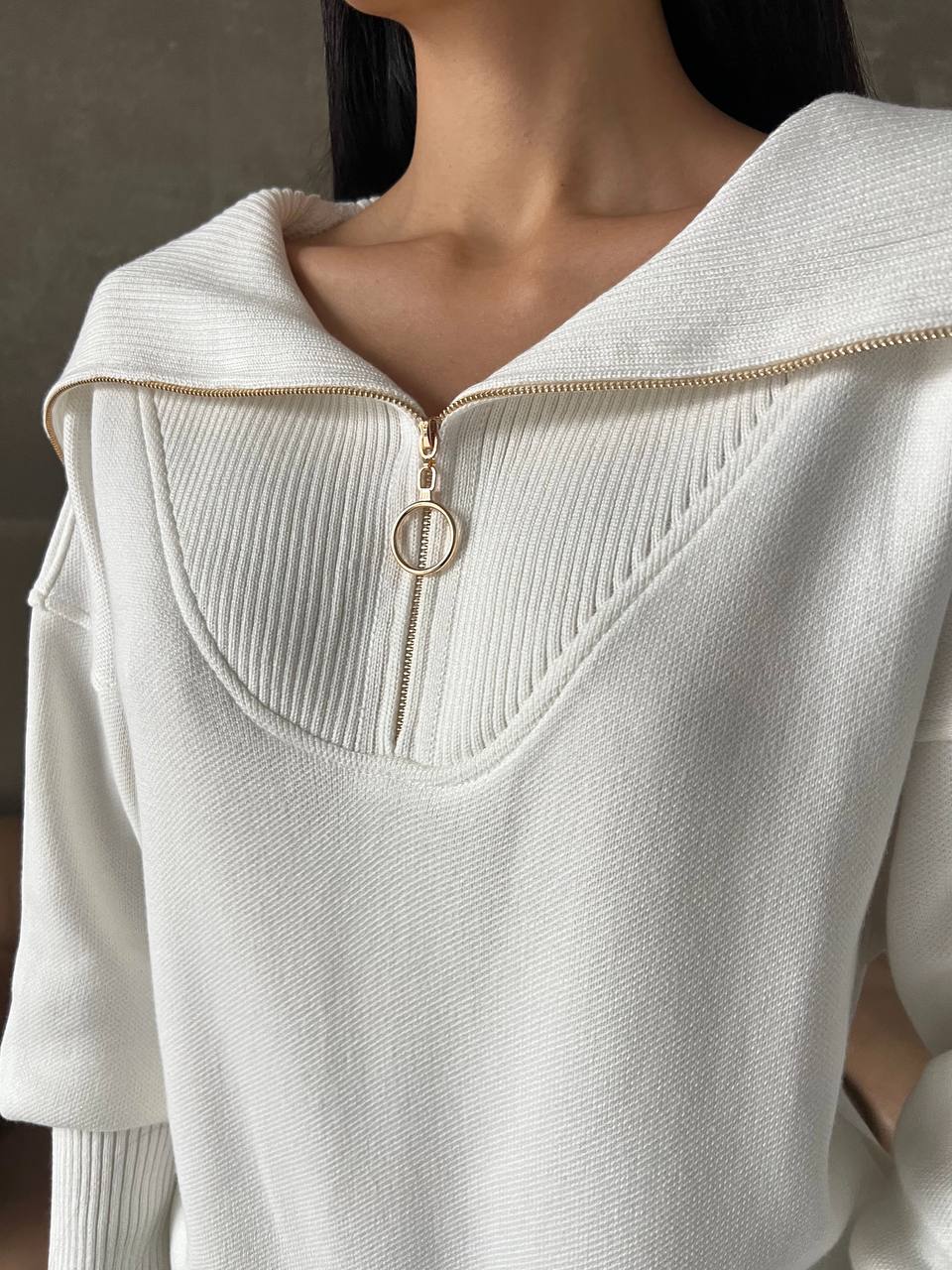 Close-up of a white sweater with a gold zipper on a dark background