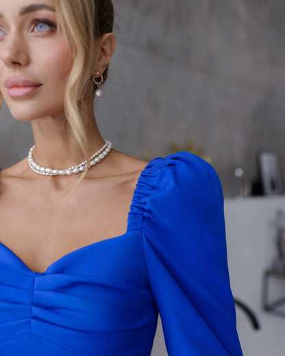 Woman wearing a blue dress with pearl necklace and earrings indoors.