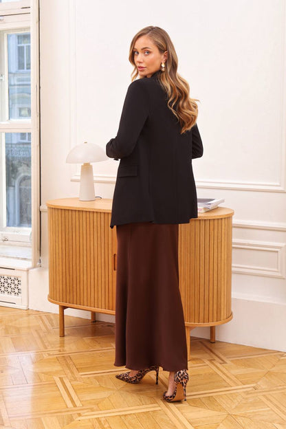 Woman in a black blazer and brown skirt standing in a room with wooden flooring and a wooden cabinet.