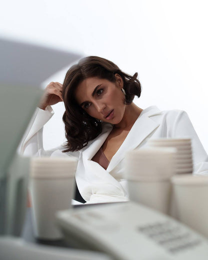 Woman in a white blazer sitting at a desk with a blurred background