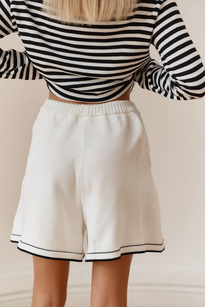 Person wearing a black and white striped long-sleeve top and white shorts on a beige background