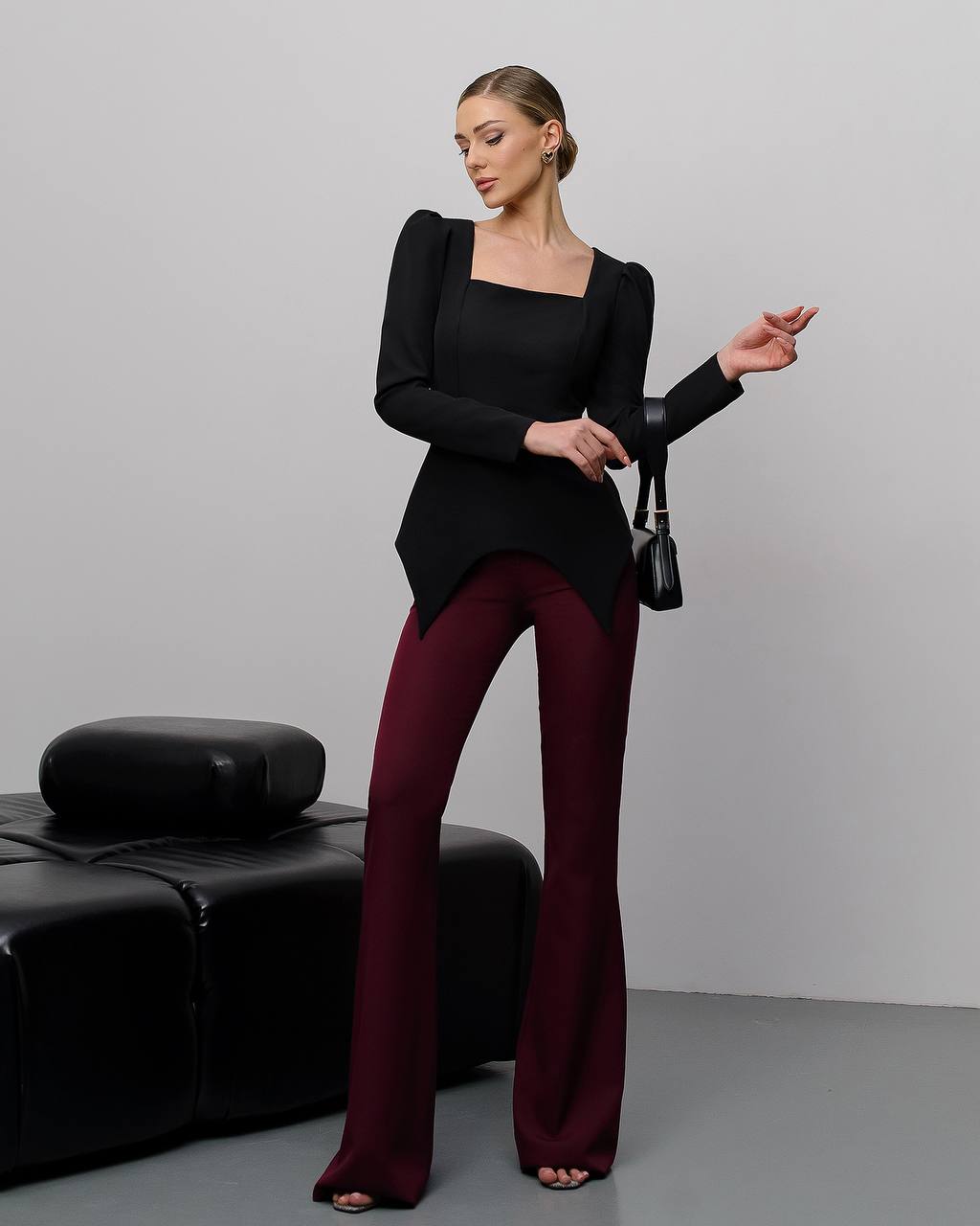 Woman wearing a black top and burgundy pants against a gray background