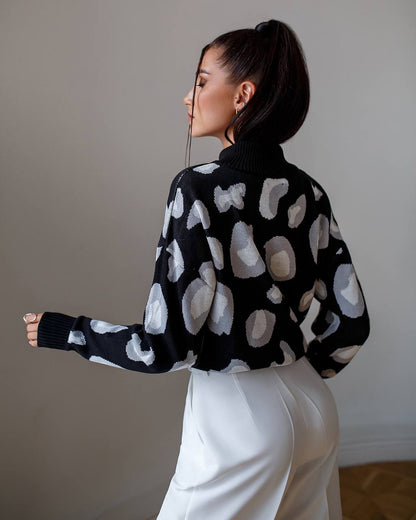Woman wearing a black sweater with white abstract patterns against a neutral background