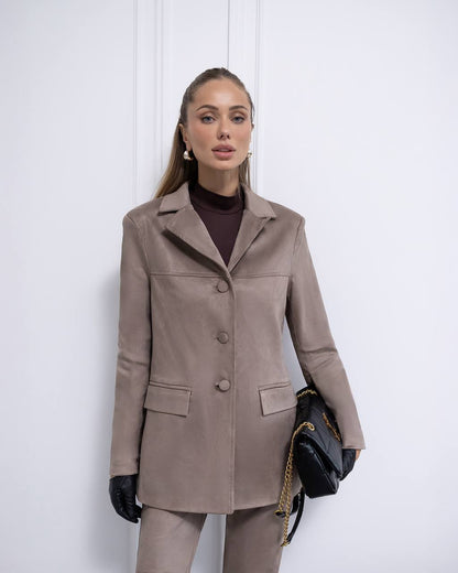 Woman wearing a brown coat and pants with a black handbag against a white background