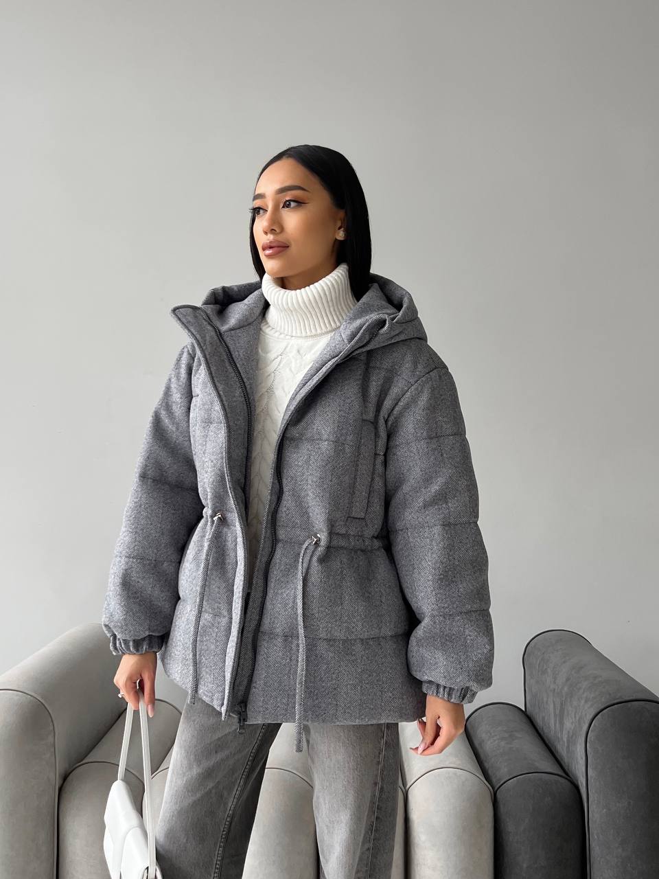 Woman wearing a gray hooded coat in a minimalistic setting