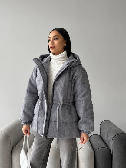 Woman wearing a gray hooded coat in a minimalistic setting