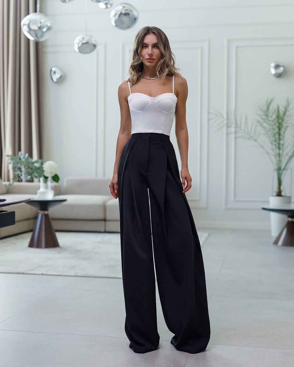 Woman wearing a white top and black wide-leg pants in a modern living room.