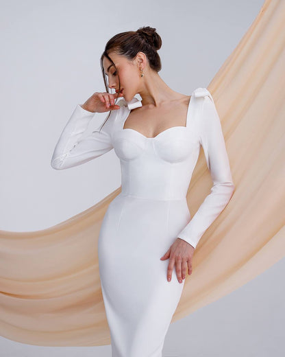 Woman wearing a white long-sleeve dress with sheer sleeves against a light background