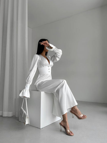 Woman in a white outfit sitting on a white cube in a minimalistic setting