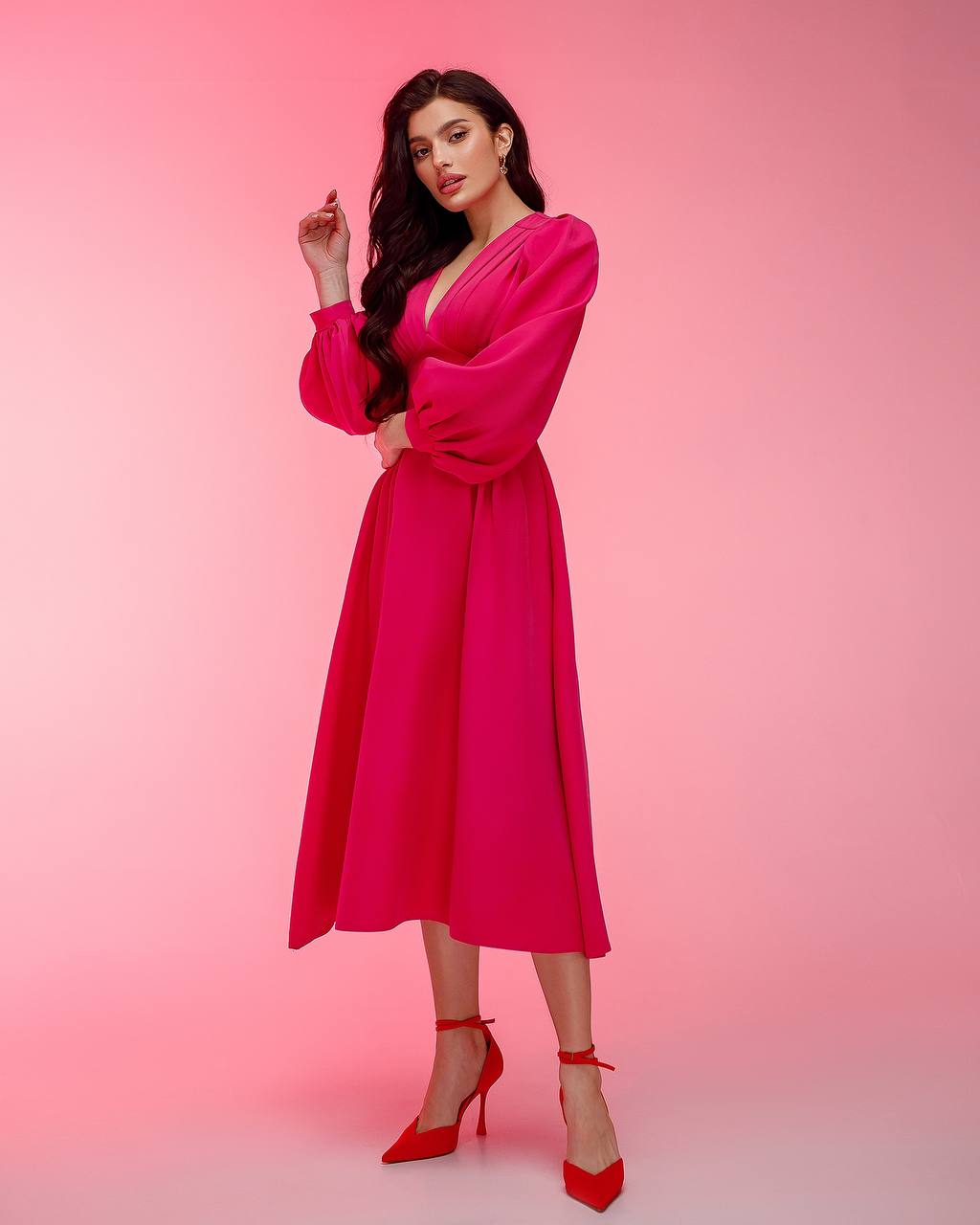 Woman wearing a bright pink dress with long sleeves against a pink background