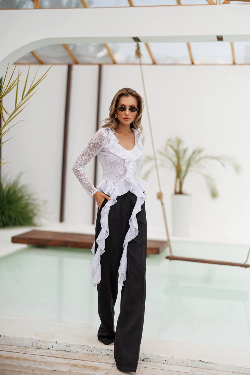 Woman wearing a white lace top and black pants with a blurred background