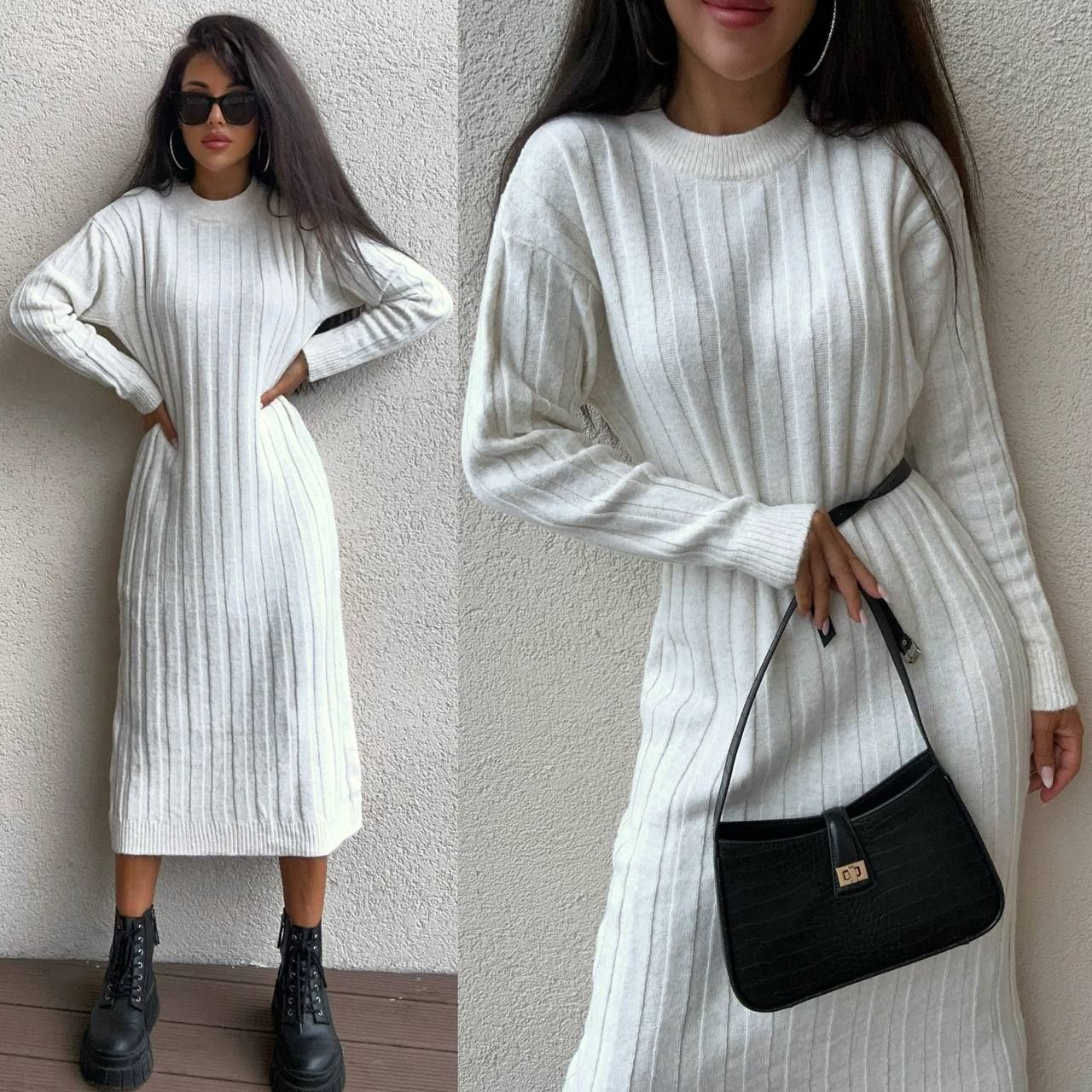 Woman wearing a white ribbed dress with black boots and a black handbag against a light gray wall.