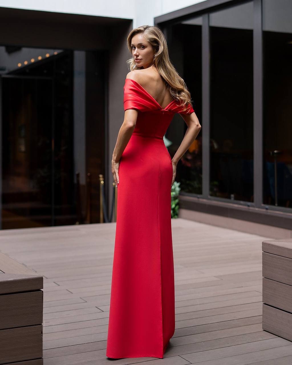 Woman in a red evening gown standing on a wooden deck.