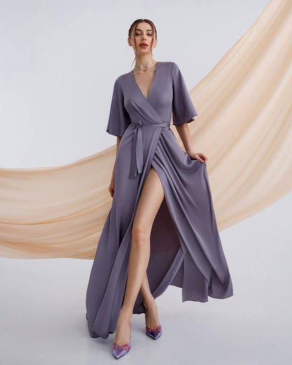 Woman wearing a long, flowing purple dress with a slit on a plain background