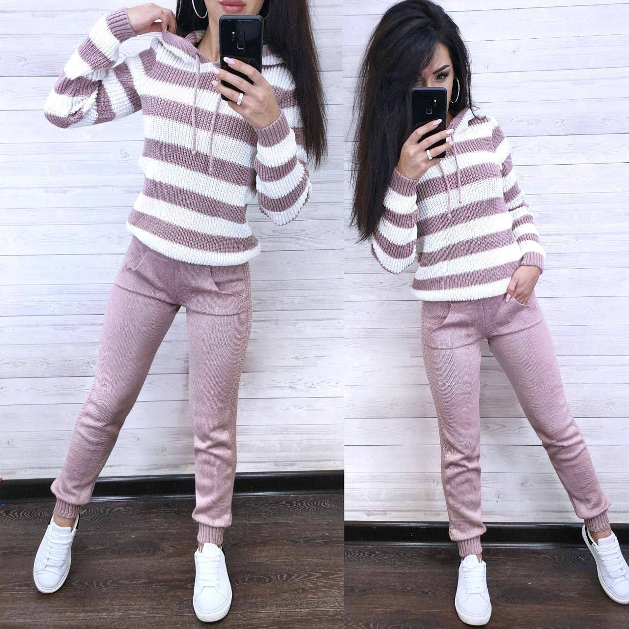 Person wearing a striped sweater and pink pants, standing in front of a white wall.