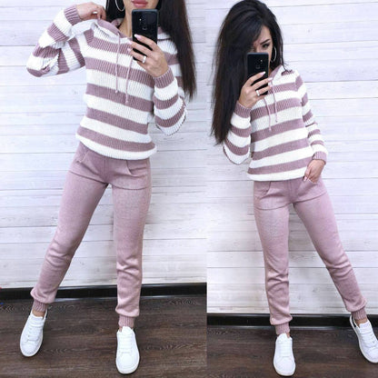 Person wearing a striped sweater and pink pants, standing in front of a white wall.