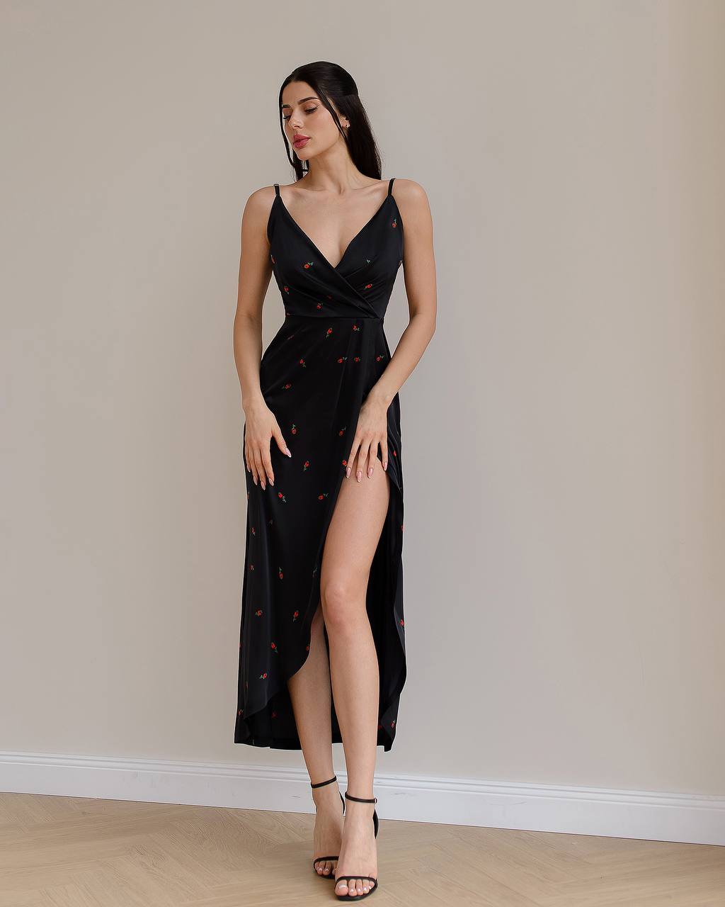 Woman wearing a black dress with a slit, standing against a plain wall.