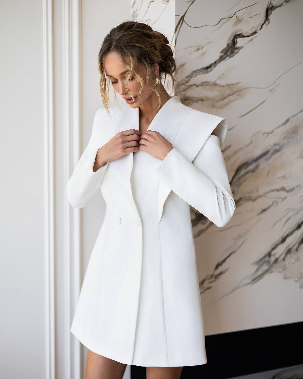 Woman wearing a white coat against a marble wall.