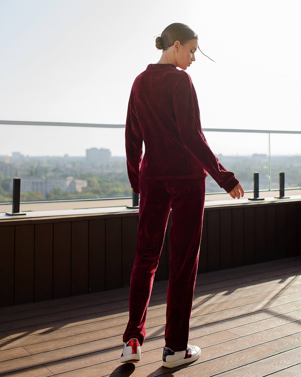 Person wearing a burgundy tracksuit standing on a rooftop with a cityscape view.
