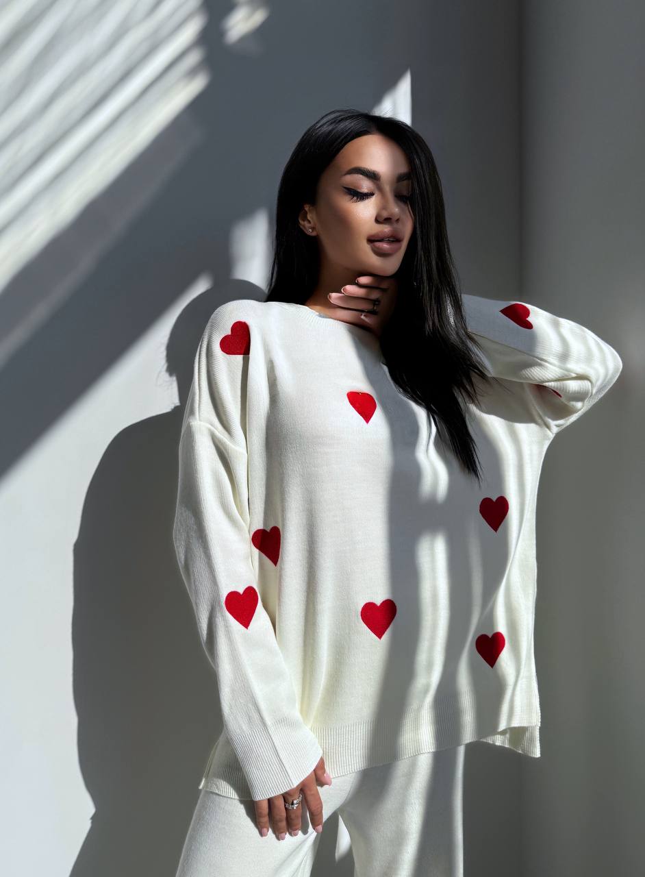 Woman wearing a white sweater with red heart patterns against a light background