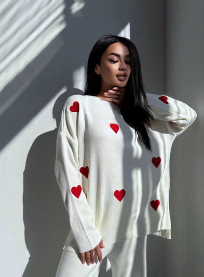 Woman wearing a white sweater with red heart patterns against a light background