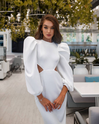Woman in a white dress with puffed sleeves standing in an indoor setting.