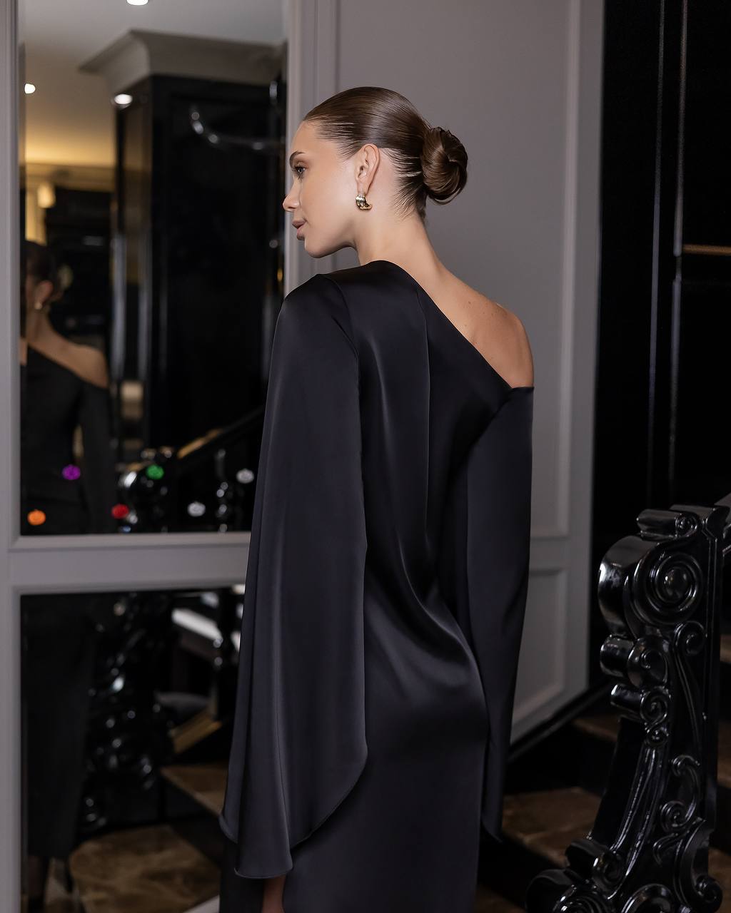 Woman wearing a black one-shoulder dress in an elegant interior setting.