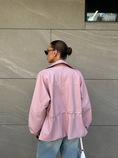 Person wearing a pink jacket standing against a gray wall