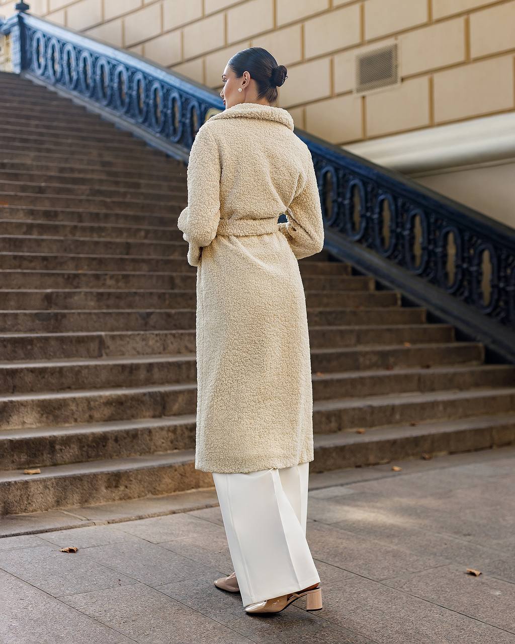 Woman in a beige coat standing on steps with a building in the background