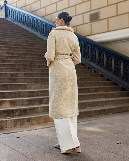 Woman in a beige coat standing on steps with a building in the background