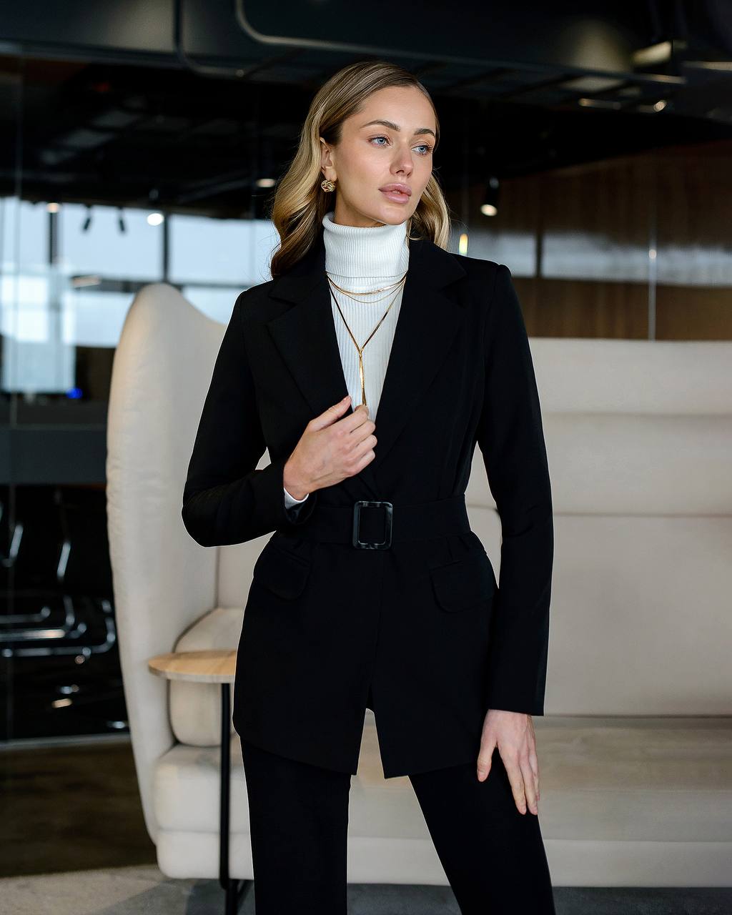 Woman in a black suit standing in an indoor setting with modern decor.