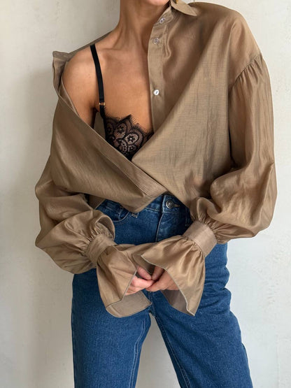 Person wearing a beige blouse with puffed sleeves and blue jeans against a neutral background