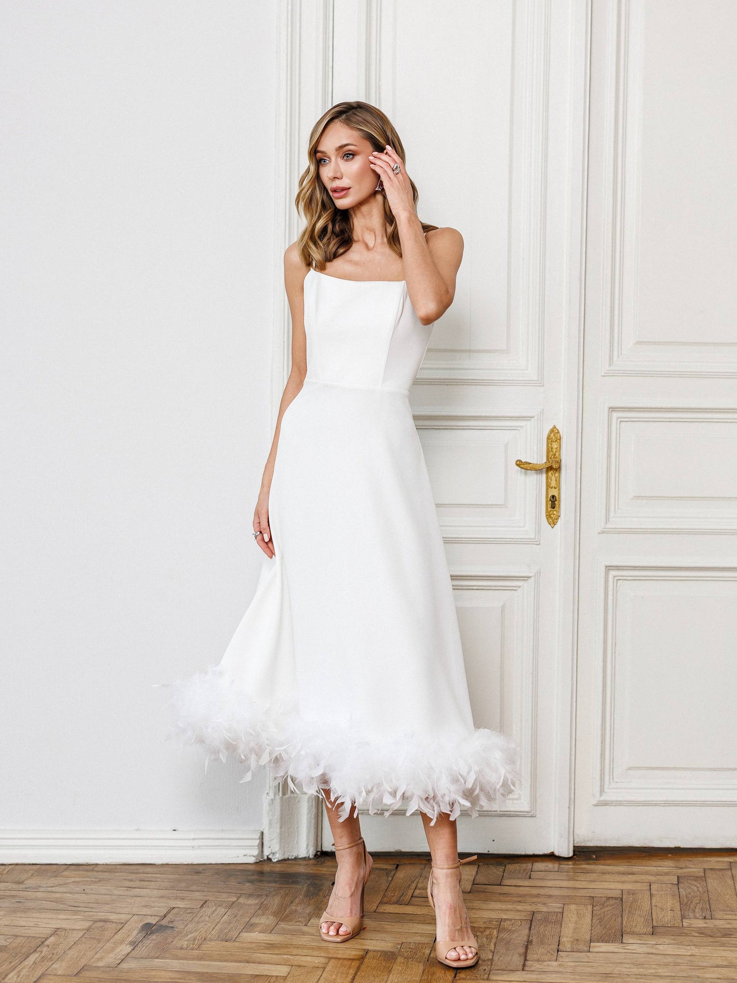 Woman in a white strapless dress standing in front of a white door.