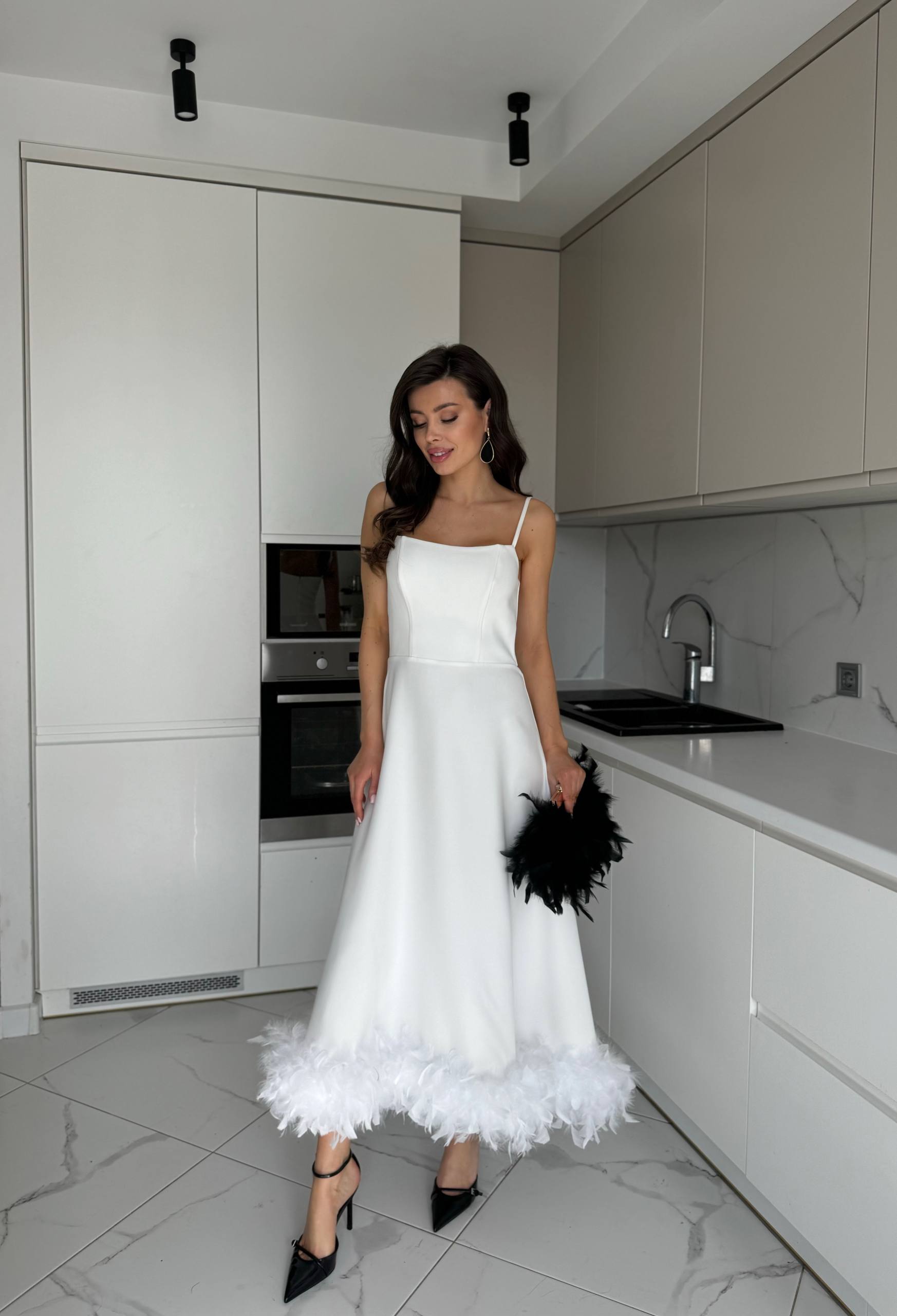 Woman in a white dress standing in a modern kitchen.