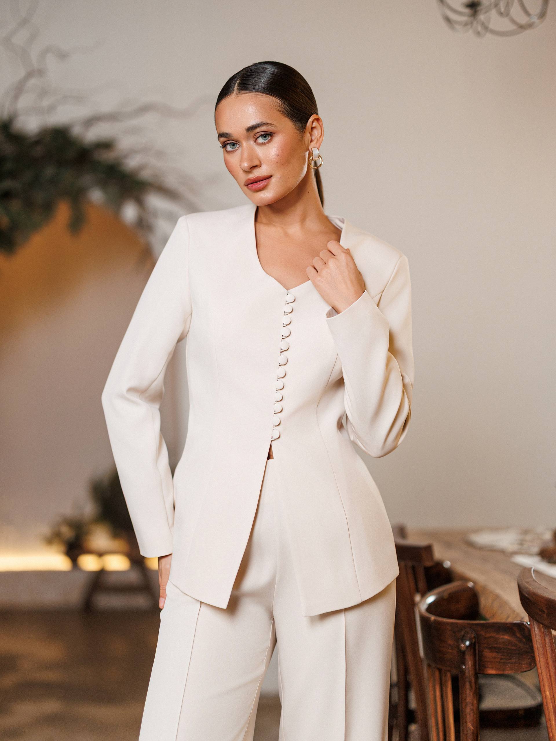 Woman wearing a cream-colored suit in an indoor setting with wooden furniture.