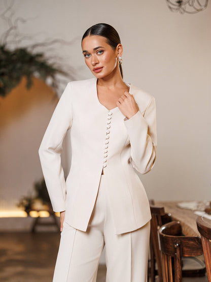 Woman wearing a cream-colored suit in an indoor setting with wooden furniture.