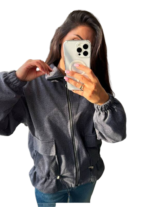 Person wearing a gray jacket taking a mirror selfie on a white background
