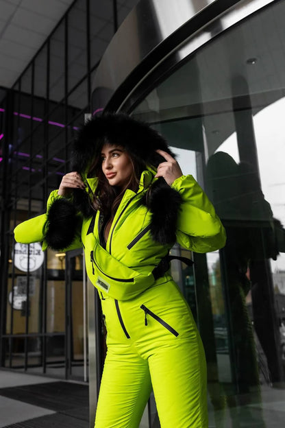 Person wearing a bright yellow snowsuit standing in front of a modern building entrance.