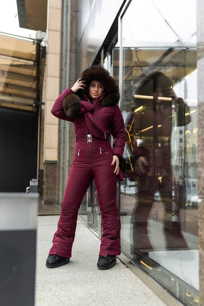 Person wearing a burgundy snowsuit with fur hood standing in front of a store window.