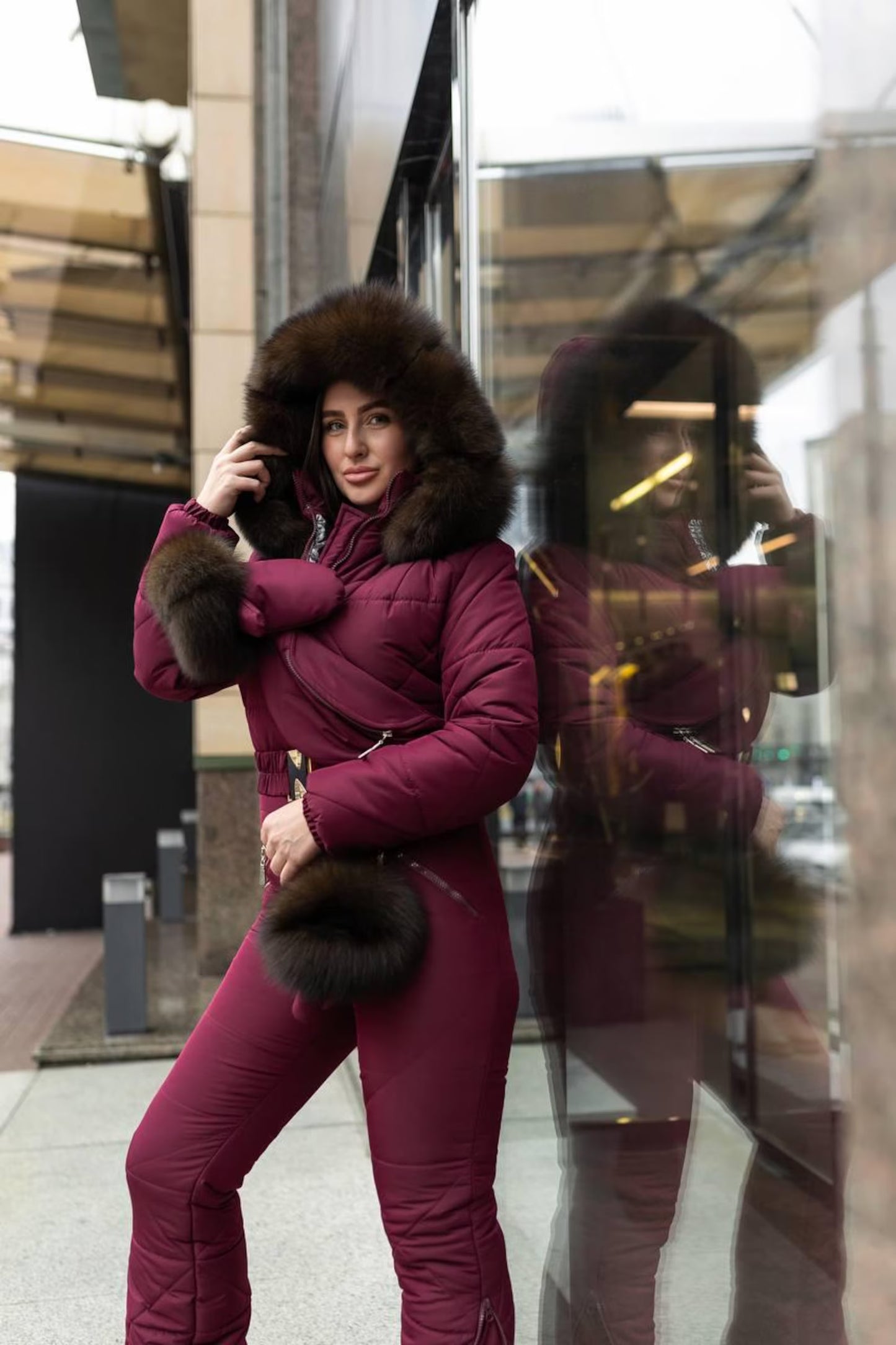 Woman in a purple winter coat with fur trim standing in front of a reflective surface.