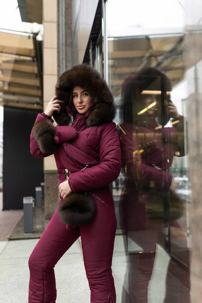 Woman in a purple winter coat with fur trim standing in front of a reflective surface.