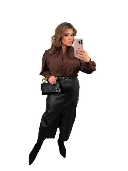 Woman taking a selfie wearing a brown blouse and black pants on a white background