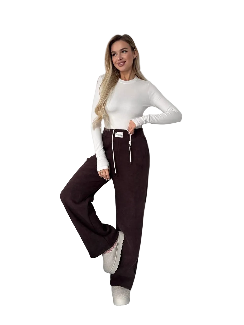 Woman wearing a white long-sleeve top and dark brown pants on a white background