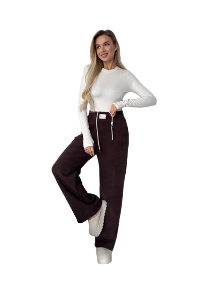 Woman wearing a white long-sleeve top and dark brown pants on a white background