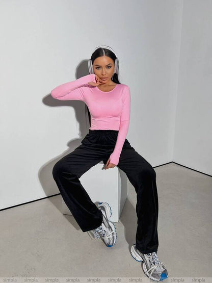 Person wearing a pink long-sleeve top and black pants sitting on a white box against a plain background.