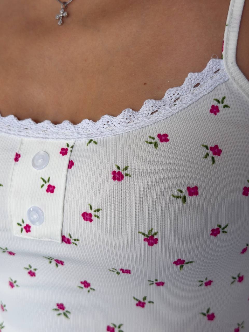 Close-up of a white ribbed camisole top with a pink and green floral print, featuring a lace-trimmed neckline and two white buttons.
