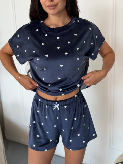 A woman wearing a navy blue two-piece pajama set with a white heart pattern, consisting of a short-sleeve crop top and matching shorts.