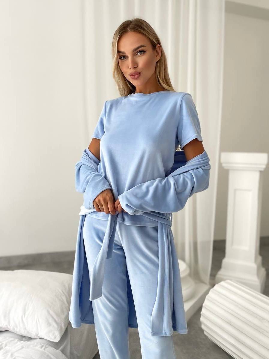 A woman modeling a light blue lounge set consisting of a short-sleeve top with long draped sleeves and matching pants, in a bright bedroom setting.