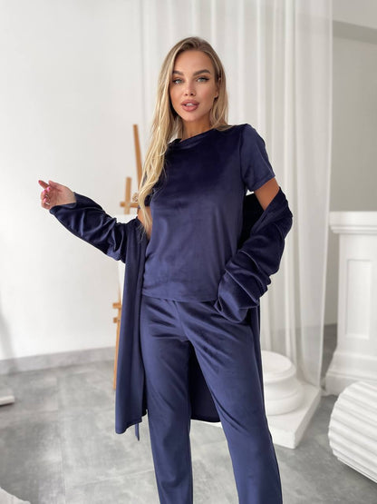 A woman modeling a matching navy blue lounge set consisting of a short-sleeve top with cutout details and matching trousers, styled with a matching long open-front cardigan in a bright, modern room.